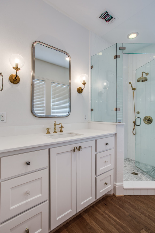 Small transitional master bathroom in Dallas with shaker cabinets, white cabinets, a corner shower, a two-piece toilet, white tile, ceramic tile, white walls, medium hardwood floors, an undermount sink, engineered quartz benchtops and a hinged shower door.