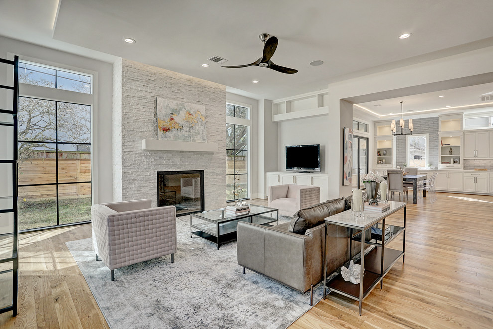 Inspiration for a transitional open concept living room in Houston with grey walls, medium hardwood floors, a standard fireplace, a stone fireplace surround, a built-in media wall and brown floor.