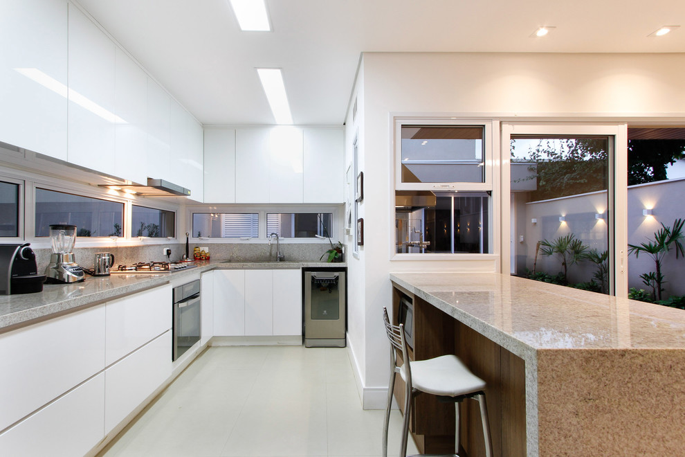 Inspiration for a mid-sized contemporary u-shaped open plan kitchen in Other with a single-bowl sink, flat-panel cabinets, white cabinets, granite benchtops, grey splashback, stone tile splashback, stainless steel appliances, porcelain floors, a peninsula, white floor and grey benchtop.