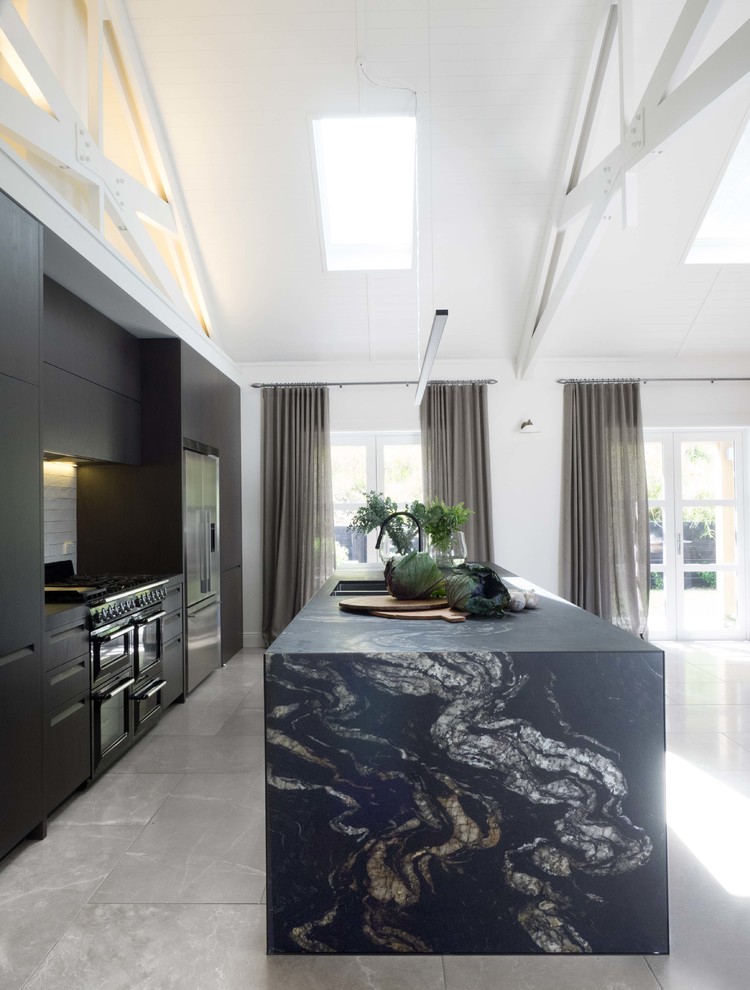 Photo of a mid-sized contemporary single-wall kitchen in Auckland with a double-bowl sink, flat-panel cabinets, dark wood cabinets, granite benchtops, white splashback, ceramic splashback, black appliances and limestone floors.