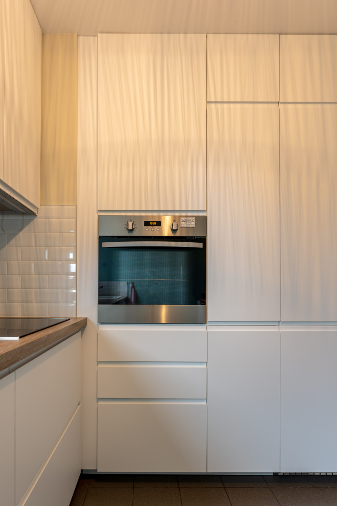 Inspiration for a small modern l-shaped separate kitchen in Paris with a single-bowl sink, flat-panel cabinets, white cabinets, laminate benchtops, white splashback, ceramic splashback and grey floor.