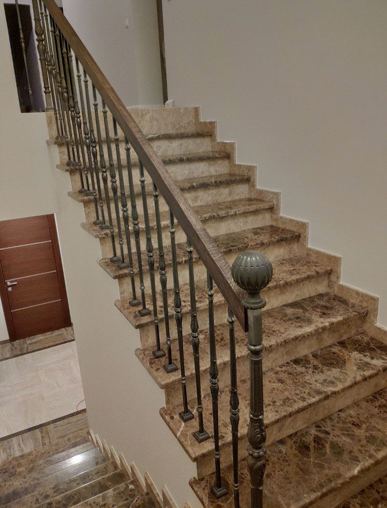 Cette image montre un escalier traditionnel en U et marbre avec des contremarches en marbre et un garde-corps en métal.
