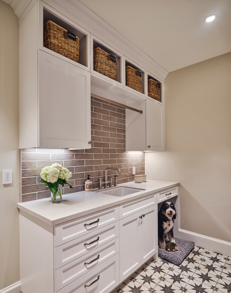 Inspiration for a mid-sized country single-wall utility room in San Francisco with an undermount sink, shaker cabinets, white cabinets, brown splashback, subway tile splashback, beige walls, porcelain floors, multi-coloured floor, white benchtop and quartz benchtops.