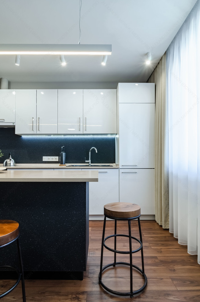 This is an example of a mid-sized contemporary galley separate kitchen in Other with a single-bowl sink, flat-panel cabinets, white cabinets, laminate benchtops, black appliances, laminate floors, with island, brown floor and beige benchtop.