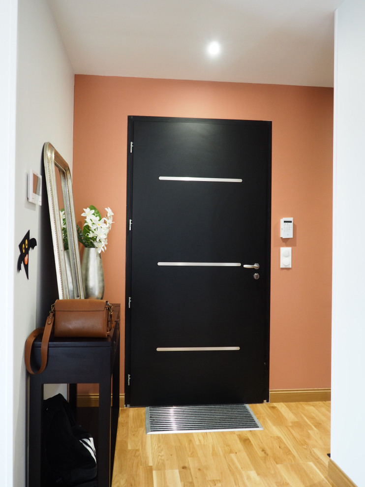 Photo of a medium sized contemporary foyer in Other with light hardwood flooring, a black front door and orange walls.