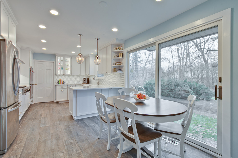 Mid-sized transitional u-shaped eat-in kitchen in Chicago with a farmhouse sink, shaker cabinets, white cabinets, marble benchtops, white splashback, stainless steel appliances, light hardwood floors, a peninsula, brown floor and white benchtop.