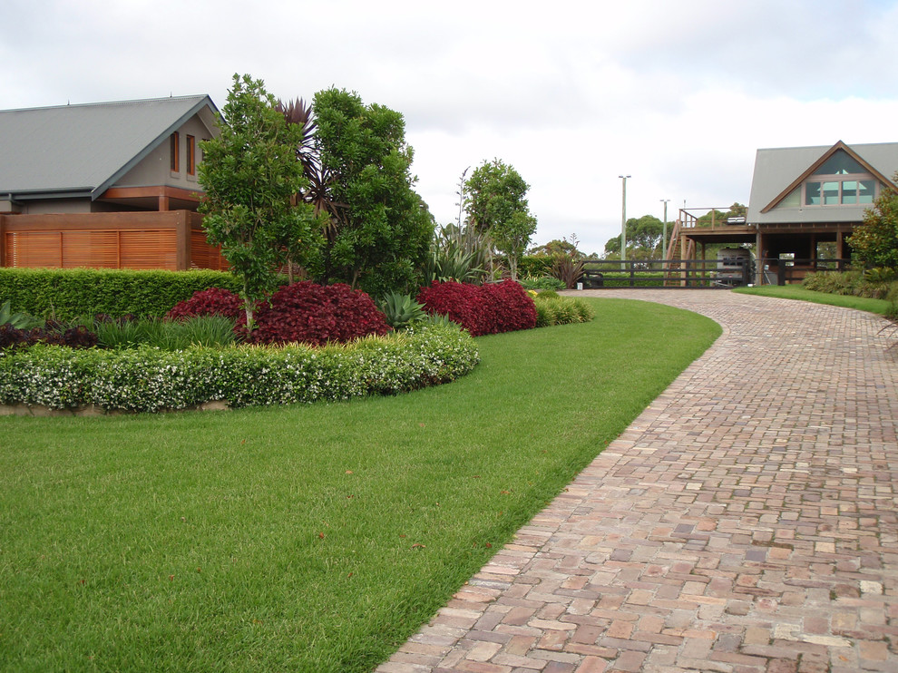 This is an example of a tropical front yard partial sun driveway for spring in Sydney with brick pavers.