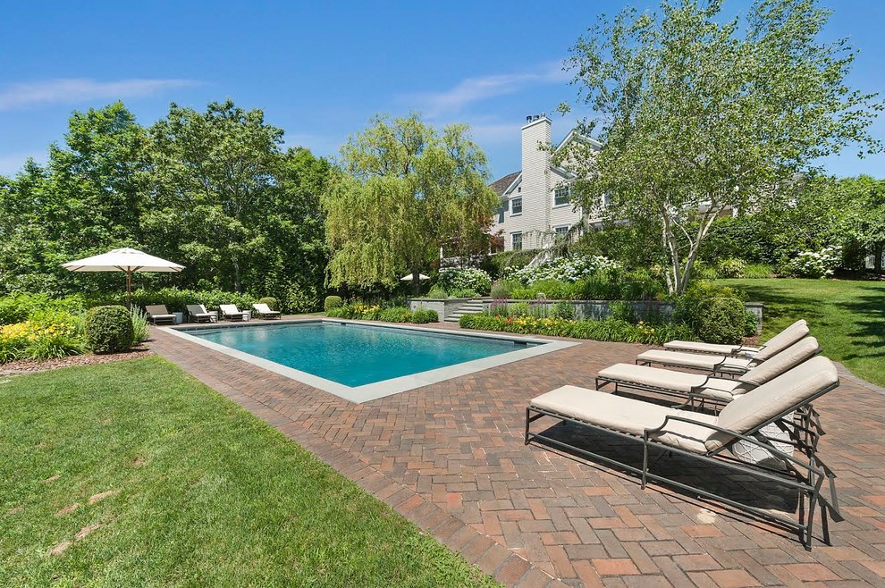 This is an example of a large beach style backyard rectangular pool in New York with brick pavers.