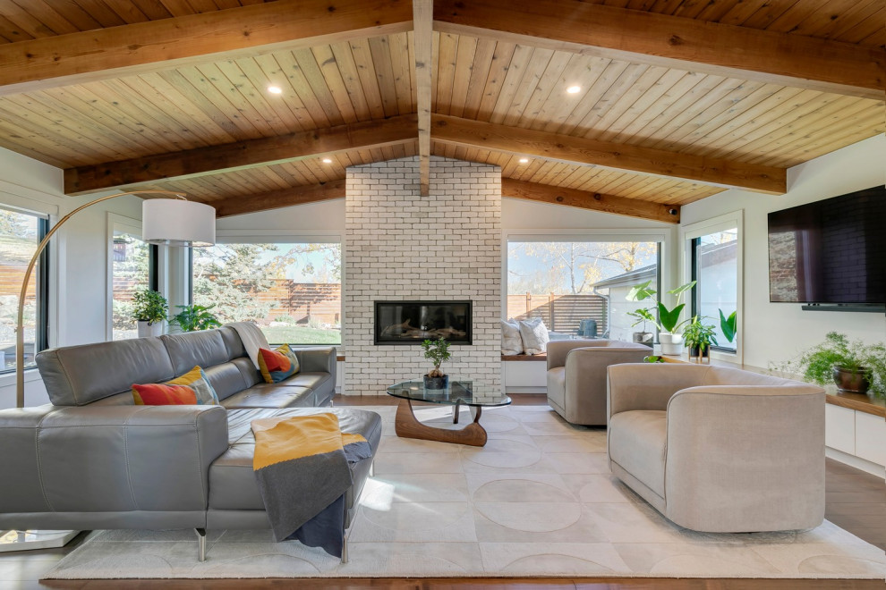 This is an example of a midcentury living room with white walls, a brick fireplace surround, brown floors and a vaulted ceiling.