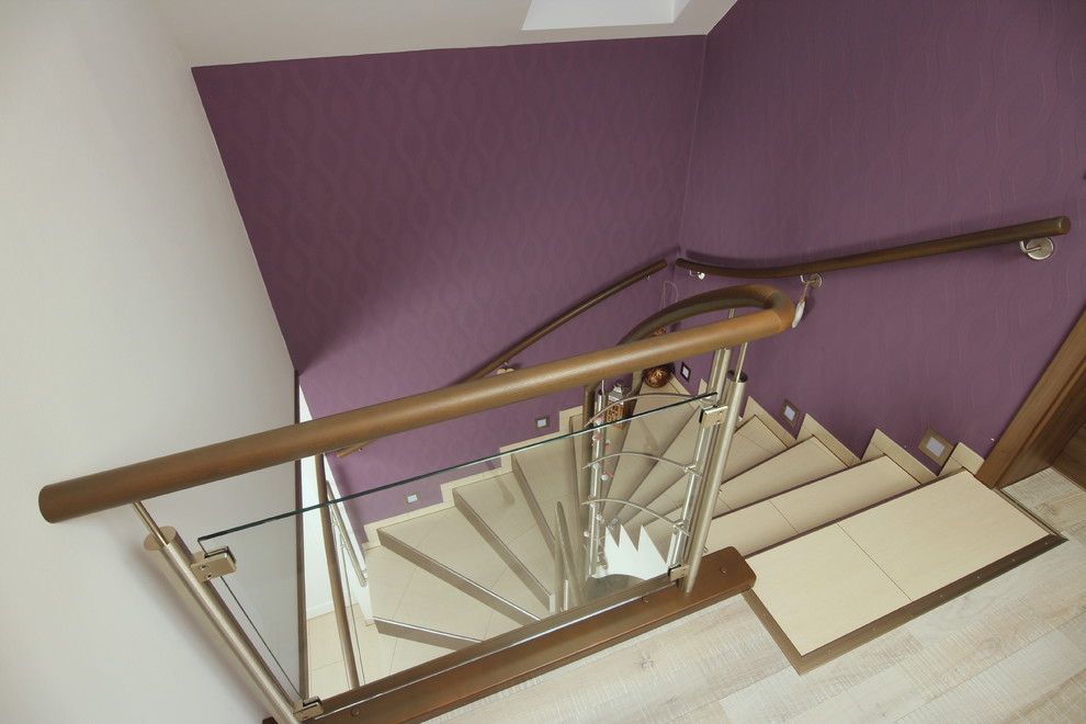 Foto på en mellanstor svängd trappa, med klinker, sättsteg i kakel och räcke i flera material