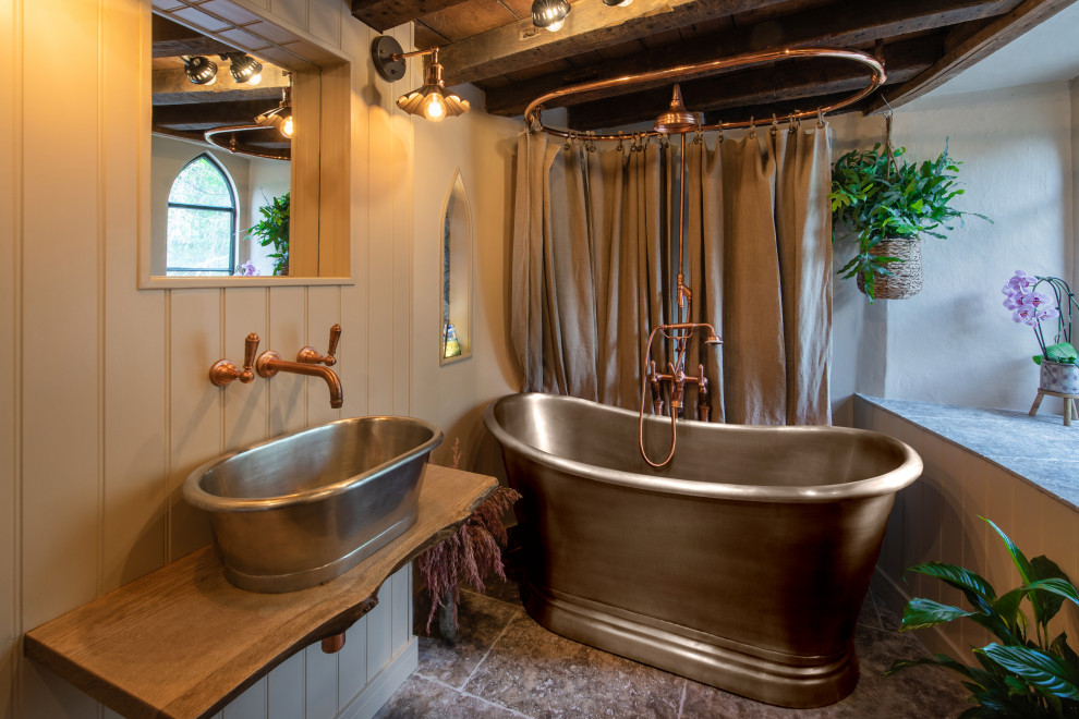 Landhausstil Badezimmer mit freistehender Badewanne, Duschbadewanne, beiger Wandfarbe, Aufsatzwaschbecken, Waschtisch aus Holz, grauem Boden, Duschvorhang-Duschabtrennung, brauner Waschtischplatte, Einzelwaschbecken und Pflanzen in Wiltshire