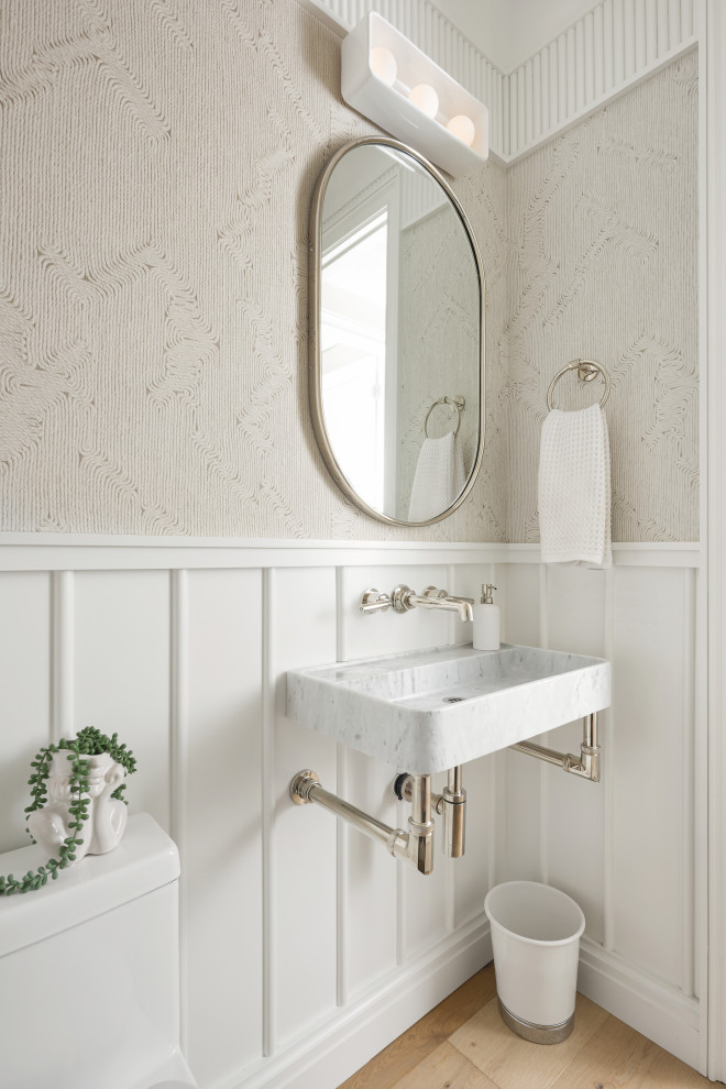 Photo of a mid-sized beach style powder room in San Diego with a wall-mount sink, marble benchtops, a floating vanity, decorative wall panelling, wallpaper, beige walls, medium hardwood floors and brown floor.