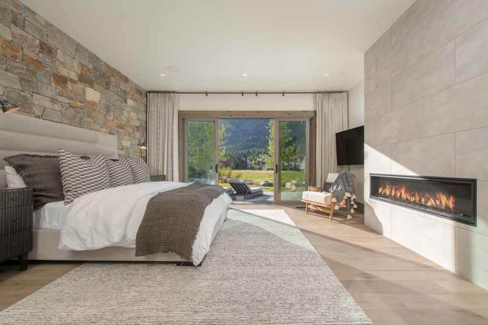 Inspiration for a country master bedroom with light hardwood floors, a standard fireplace, a concrete fireplace surround and brown floor.
