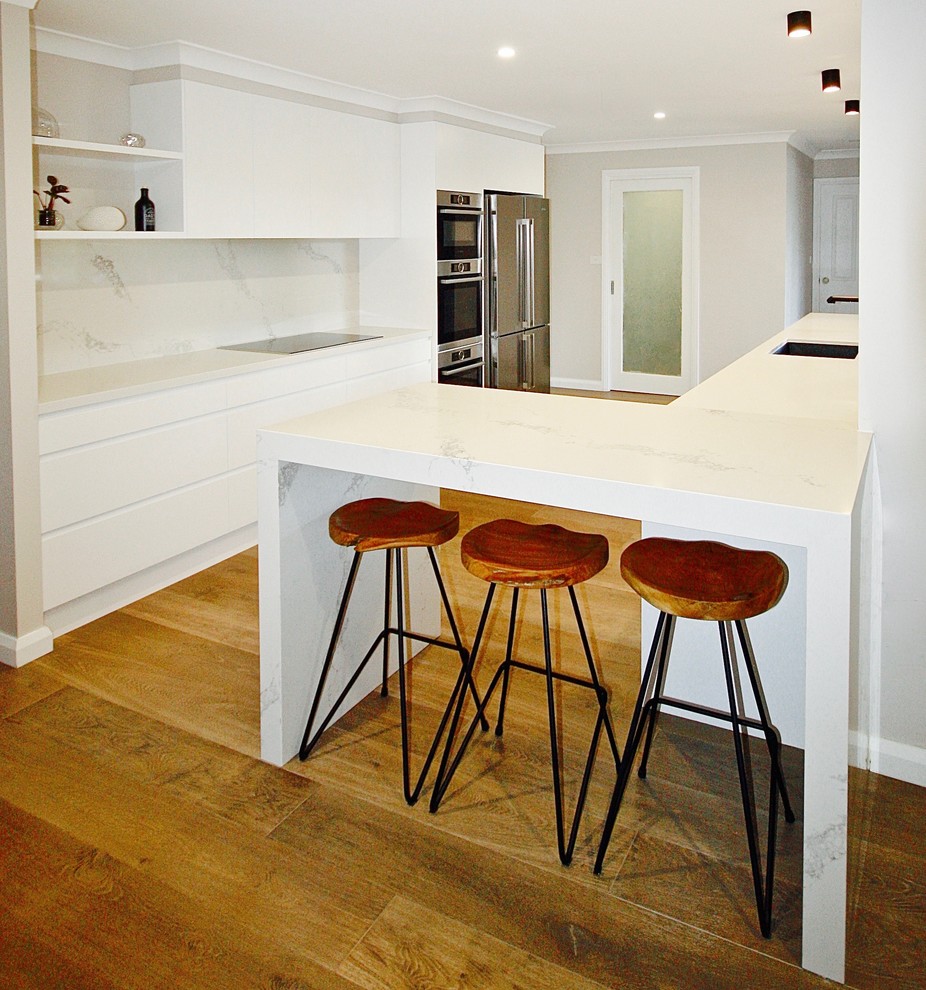 Design ideas for a mid-sized contemporary galley kitchen pantry in Sydney with a drop-in sink, flat-panel cabinets, white cabinets, quartz benchtops, white splashback, stone slab splashback, stainless steel appliances, medium hardwood floors and no island.