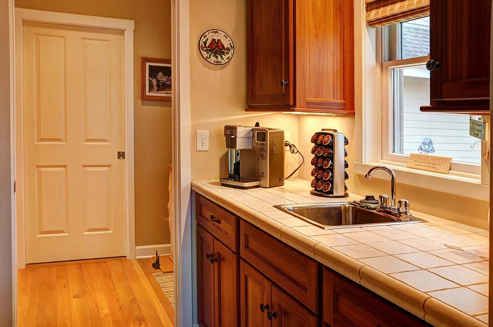 Mid-sized mountain style galley medium tone wood floor kitchen pantry photo in Milwaukee with a drop-in sink, recessed-panel cabinets, medium tone wood cabinets and tile countertops