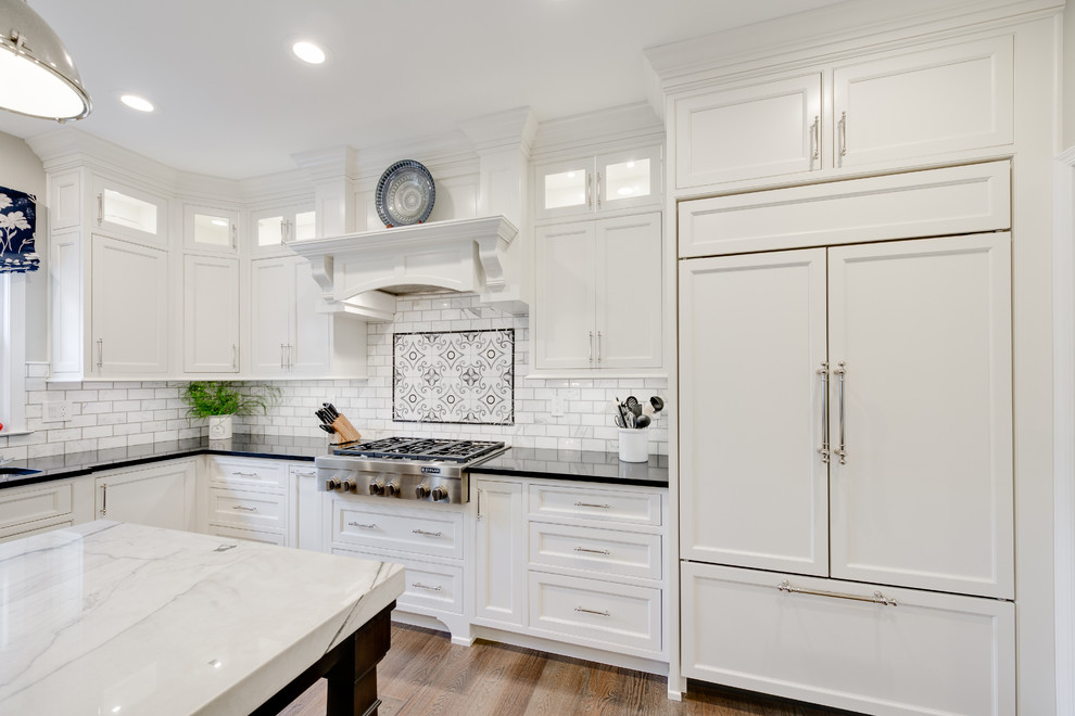 This is an example of a large transitional u-shaped eat-in kitchen in Philadelphia with an undermount sink, recessed-panel cabinets, white cabinets, quartz benchtops, white splashback, subway tile splashback, panelled appliances, medium hardwood floors, with island, brown floor and black benchtop.