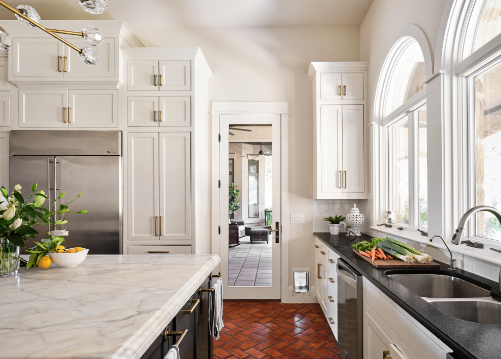 This is an example of an expansive traditional u-shaped kitchen in Austin with an undermount sink, shaker cabinets, white cabinets, marble benchtops, white splashback, subway tile splashback, stainless steel appliances, brick floors and with island.