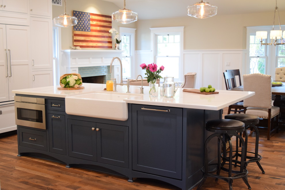 Arts and crafts l-shaped open plan kitchen in San Diego with a farmhouse sink, shaker cabinets, blue cabinets, quartz benchtops, white splashback, marble splashback, panelled appliances, light hardwood floors and with island.