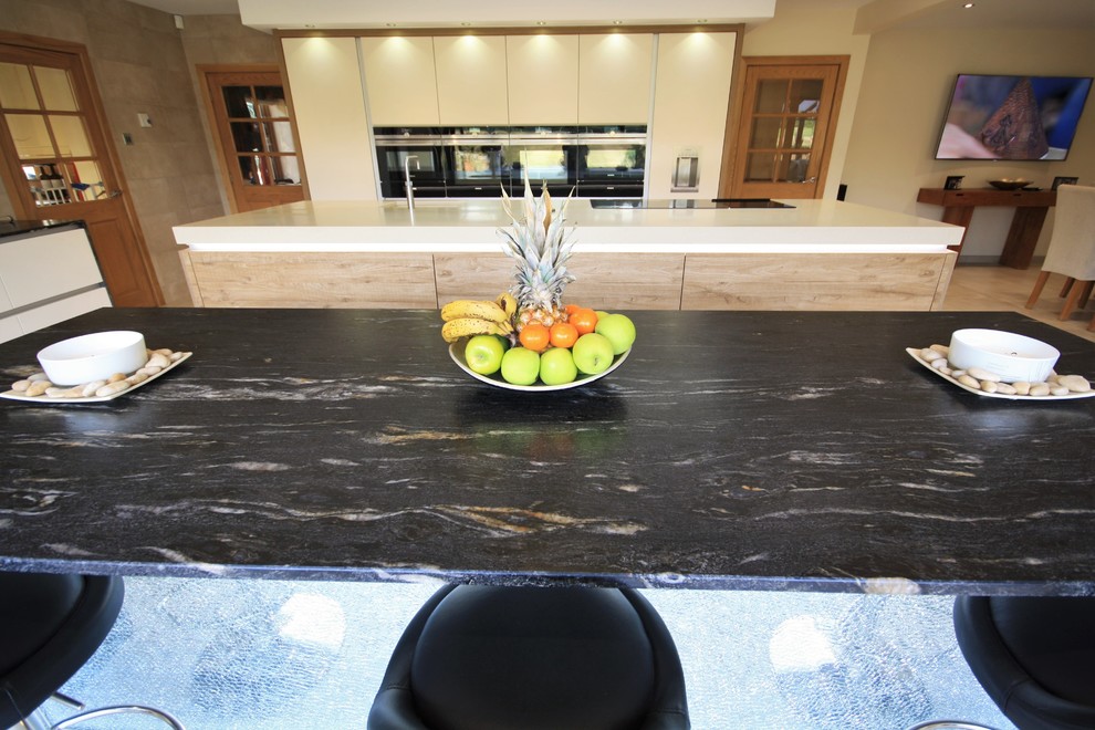 Photo of a large contemporary kitchen in Essex with flat-panel cabinets, black appliances, porcelain floors and multiple islands.
