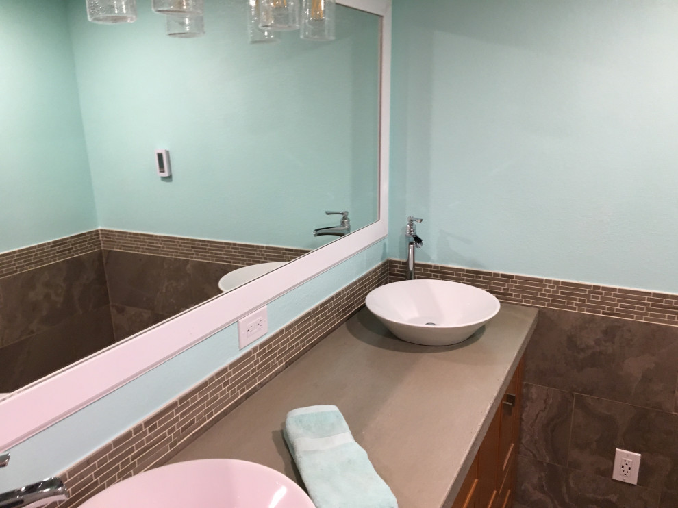 Photo of a large modern master bathroom in Orlando with shaker cabinets, medium wood cabinets, a freestanding tub, a double shower, a two-piece toilet, brown tile, limestone, blue walls, limestone floors, a vessel sink, concrete benchtops, brown floor, a sliding shower screen and grey benchtops.