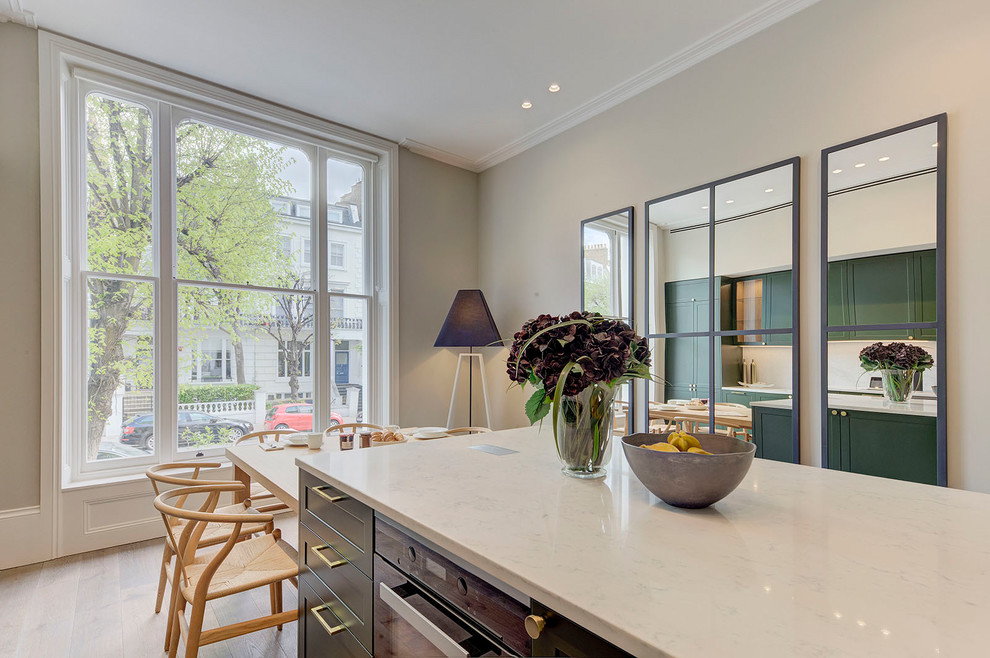 Photo of a mid-sized transitional single-wall eat-in kitchen in London with shaker cabinets, green cabinets, white splashback, marble splashback, stainless steel appliances, light hardwood floors, with island, beige floor and white benchtop.