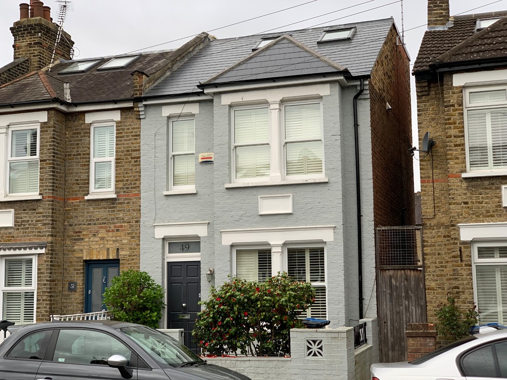 Small traditional three-storey brick blue townhouse exterior in London with a gable roof and a tile roof.