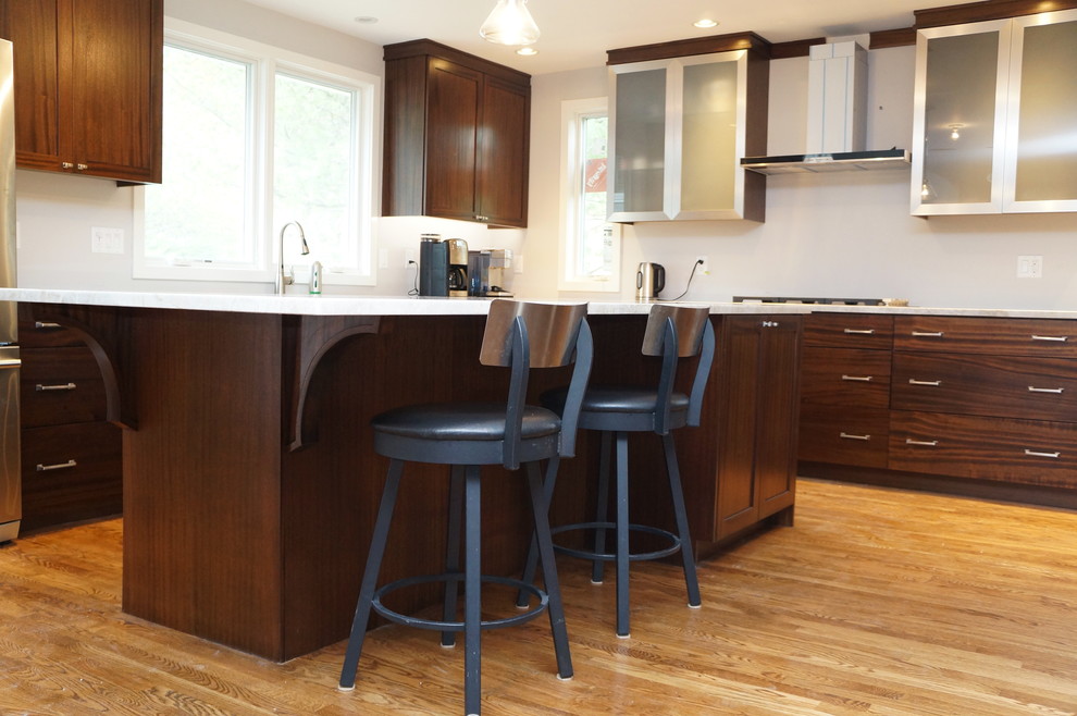 Photo of an expansive contemporary u-shaped eat-in kitchen in Boston with flat-panel cabinets, dark wood cabinets, marble benchtops, white splashback, stainless steel appliances, light hardwood floors, with island, a drop-in sink, brown floor and white benchtop.