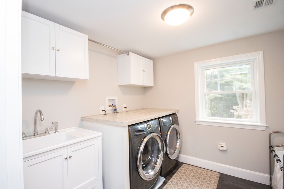 This is an example of a mid-sized transitional single-wall dedicated laundry room in Boston with a drop-in sink, recessed-panel cabinets, white cabinets, laminate benchtops, grey walls, vinyl floors, a side-by-side washer and dryer, grey floor and brown benchtop.