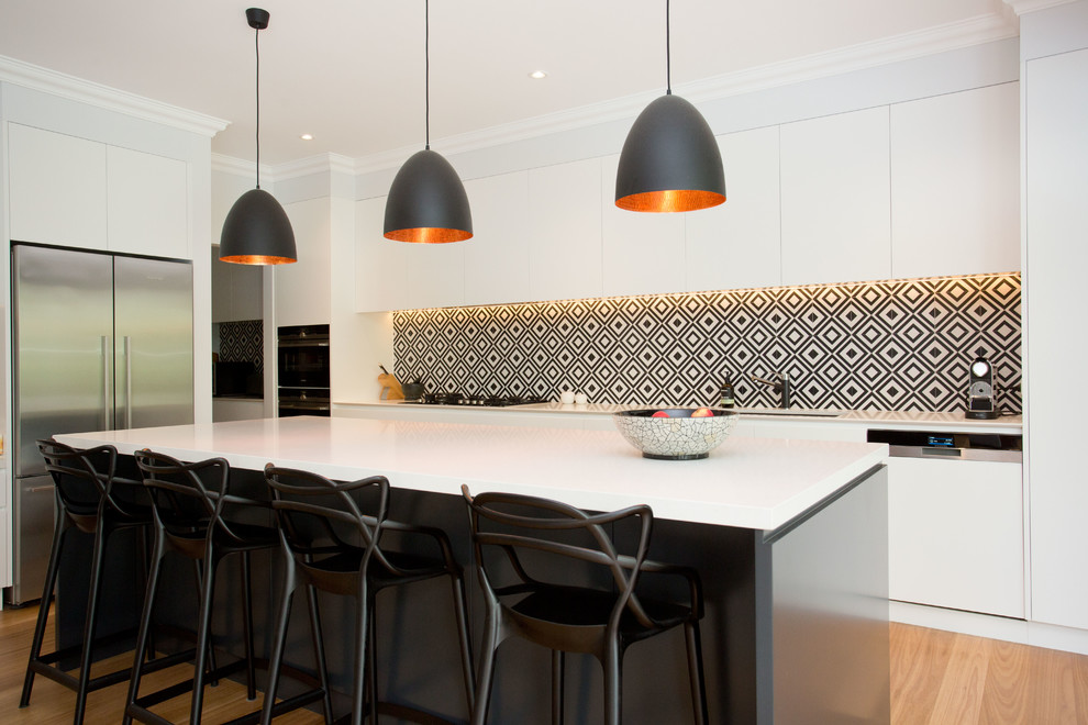 Inspiration for a contemporary l-shaped kitchen in Sydney with white cabinets, solid surface benchtops, multi-coloured splashback, ceramic splashback, with island, white benchtop, an undermount sink, flat-panel cabinets, stainless steel appliances, light hardwood floors and beige floor.