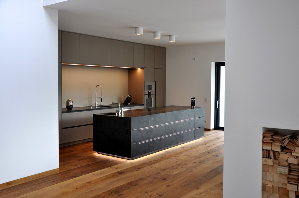 Photo of a mid-sized contemporary galley open plan kitchen in Munich with flat-panel cabinets, with island, beige splashback, a drop-in sink, grey cabinets and light hardwood floors.
