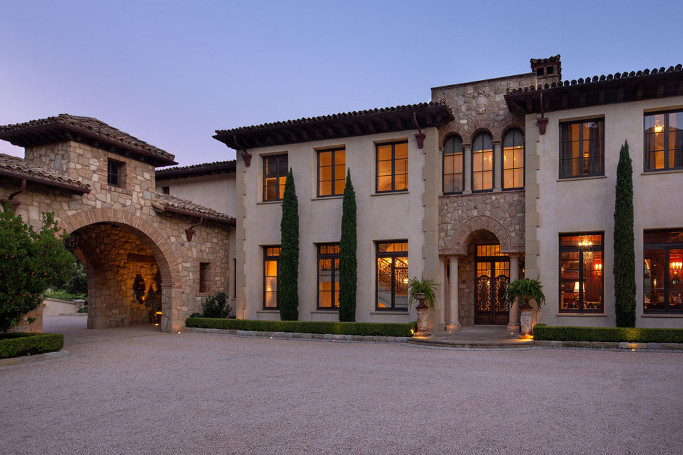 This is an example of an expansive mediterranean two-storey beige house exterior in Santa Barbara with stone veneer and a tile roof.