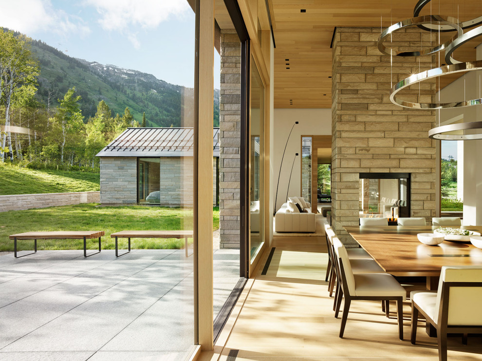 Réalisation d'une salle à manger minimaliste avec une cheminée double-face, un manteau de cheminée en pierre et un plafond en bois.