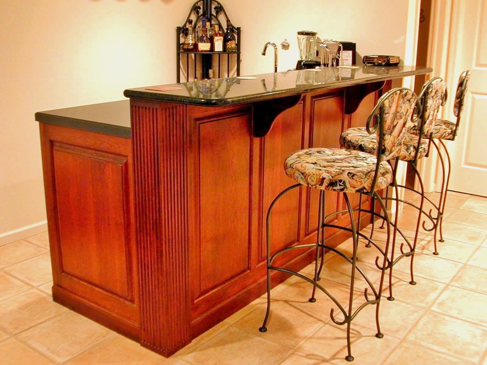 Inspiration for a small traditional single-wall home bar in New York with a drop-in sink, raised-panel cabinets, medium wood cabinets, granite benchtops, terra-cotta floors and beige floor.