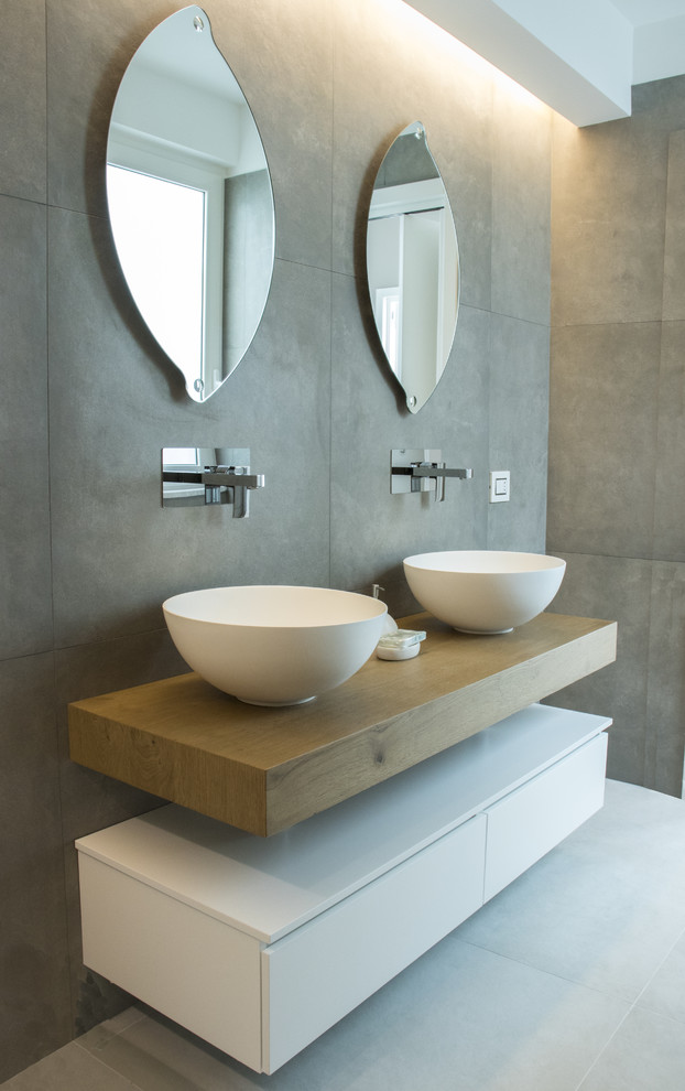 Contemporary master bathroom in Bari with gray tile, porcelain tile, a vessel sink, flat-panel cabinets, white cabinets, grey walls, wood benchtops, white floor and brown benchtops.