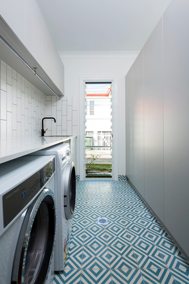 This is an example of a small traditional galley dedicated laundry room in Brisbane with a double-bowl sink, flat-panel cabinets, white cabinets, solid surface benchtops, white walls, porcelain floors, a side-by-side washer and dryer and multi-coloured floor.