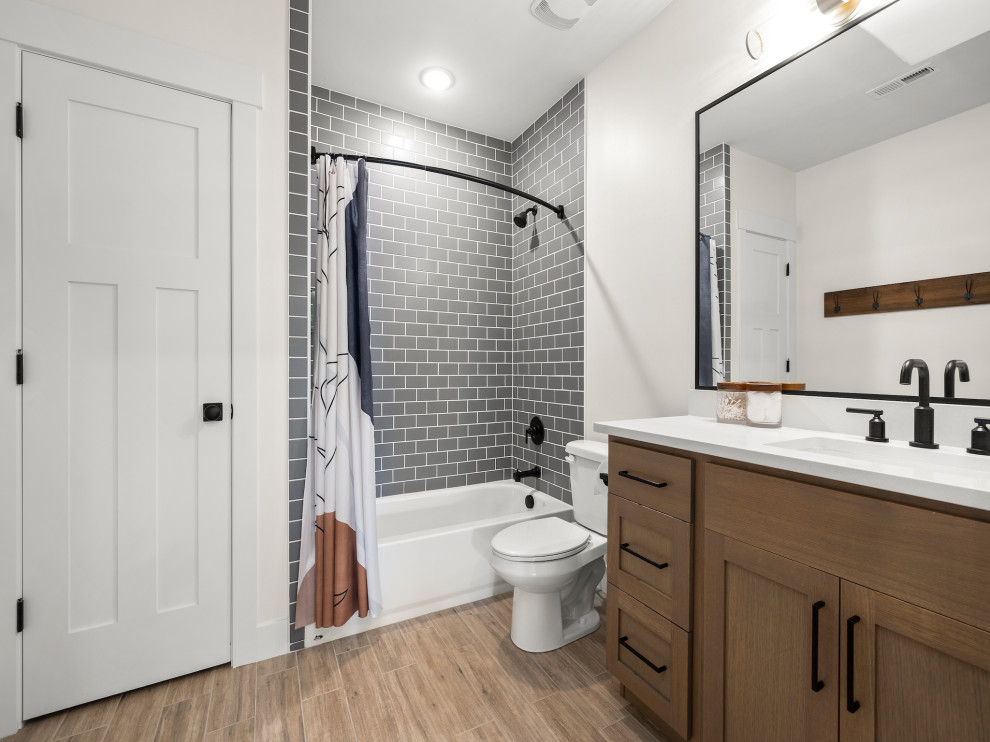This is an example of a mid-sized transitional bathroom in Other with shaker cabinets, light wood cabinets, a drop-in tub, a shower/bathtub combo, a one-piece toilet, gray tile, ceramic tile, white walls, an undermount sink, engineered quartz benchtops, brown floor, a shower curtain, white benchtops, a single vanity, a built-in vanity and wood-look tile.