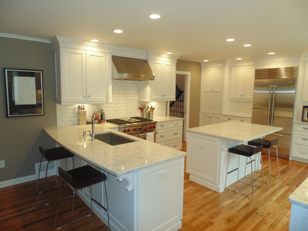 Inspiration for a large transitional u-shaped medium tone wood floor and brown floor eat-in kitchen remodel with an undermount sink, recessed-panel cabinets, white cabinets, quartz countertops, white backsplash, subway tile backsplash, stainless steel appliances, an island and white countertops