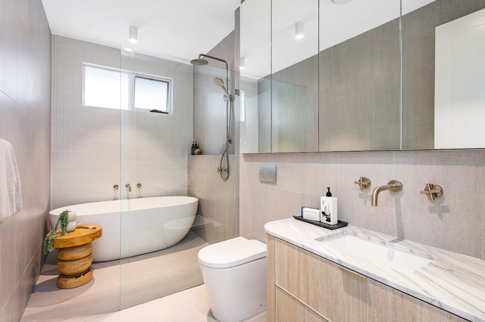 This is an example of a mid-sized modern master bathroom in Sydney with beaded inset cabinets, light wood cabinets, a freestanding tub, a shower/bathtub combo, a one-piece toilet, gray tile, ceramic tile, grey walls, ceramic floors, an undermount sink, engineered quartz benchtops, grey floor, an open shower, white benchtops, a single vanity and a floating vanity.