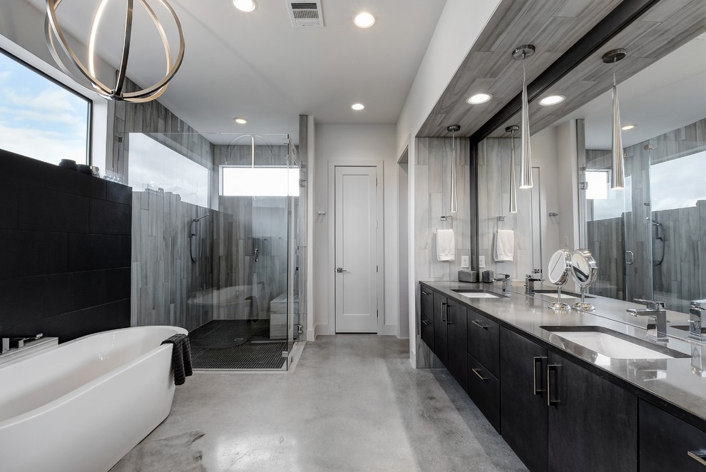 Mid-sized contemporary master bathroom in Austin with flat-panel cabinets, a freestanding tub, a corner shower, gray tile, porcelain tile, concrete floors, an undermount sink, engineered quartz benchtops, grey floor, a hinged shower door, grey benchtops and black cabinets.