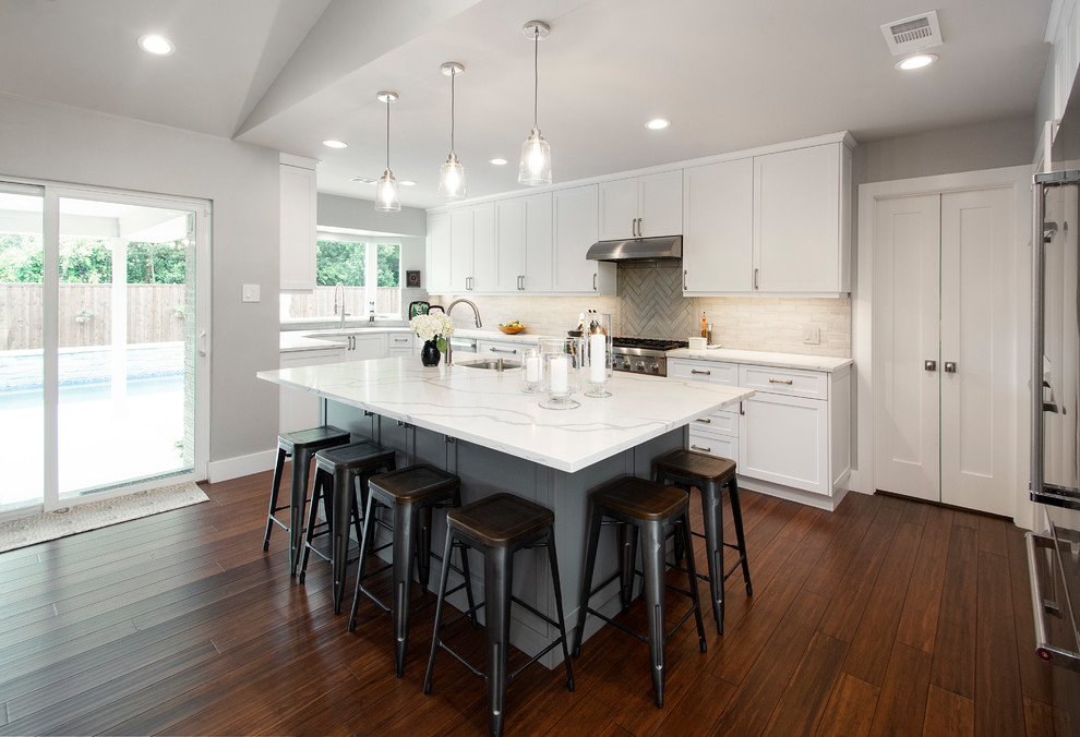 Design ideas for a mid-sized transitional l-shaped eat-in kitchen in Dallas with an undermount sink, flat-panel cabinets, white cabinets, quartz benchtops, grey splashback, ceramic splashback, stainless steel appliances, medium hardwood floors, with island, brown floor and white benchtop.