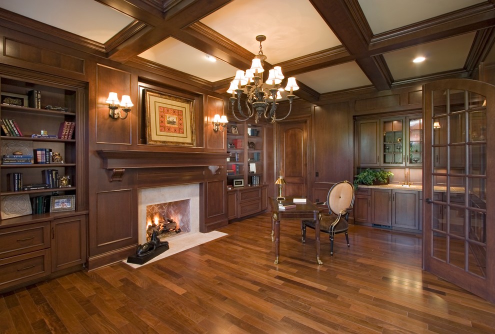 Photo of an expansive traditional study room in St Louis with brown walls, dark hardwood floors, a standard fireplace, a stone fireplace surround, a freestanding desk and brown floor.