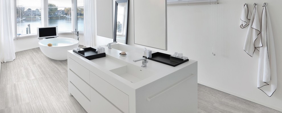 Design ideas for a mid-sized contemporary master bathroom in Denver with flat-panel cabinets, white cabinets, a freestanding tub, white walls, porcelain floors, an integrated sink, solid surface benchtops, grey floor, white tile, white benchtops and a double vanity.