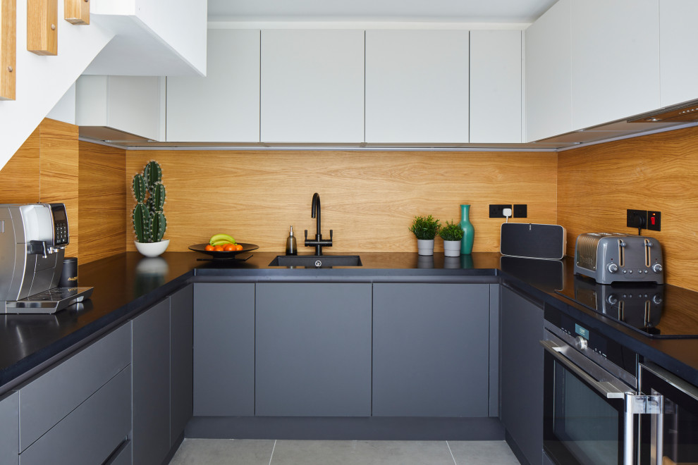 Inspiration for an industrial u-shaped kitchen in London with an undermount sink, flat-panel cabinets, grey cabinets, brown splashback, timber splashback, black appliances, no island, grey floor and black benchtop.
