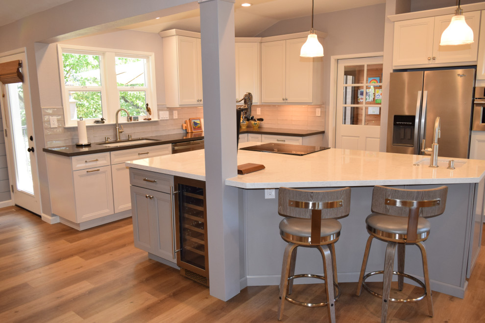 This is an example of a mid-sized transitional l-shaped eat-in kitchen in Sacramento with an undermount sink, shaker cabinets, white cabinets, quartz benchtops, grey splashback, ceramic splashback, stainless steel appliances, vinyl floors, with island, brown floor, grey benchtop and vaulted.