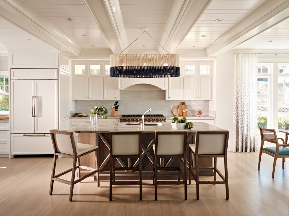 Cette photo montre une cuisine américaine encastrable bord de mer avec un placard avec porte à panneau encastré, des portes de placard blanches, une crédence grise, un sol en bois brun, îlot et un plafond en lambris de bois.