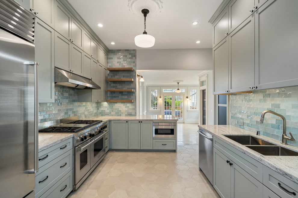 Klassisk inredning av ett stort grå grått kök, med en dubbel diskho, luckor med infälld panel, grå skåp, granitbänkskiva, grönt stänkskydd, stänkskydd i glaskakel, rostfria vitvaror, en köksö, klinkergolv i keramik och beiget golv