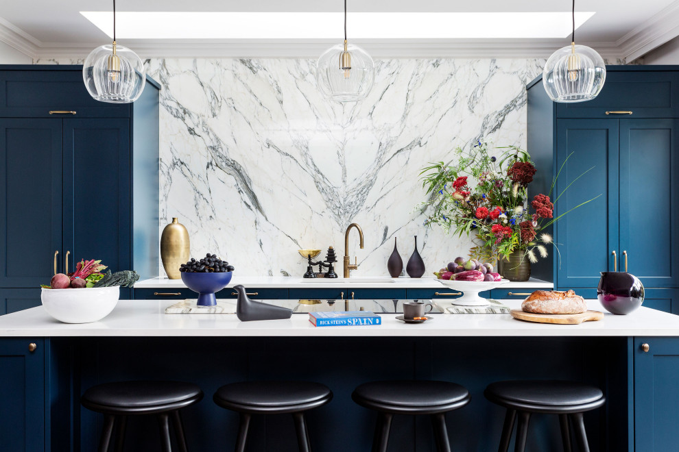 Immagine di un grande cucina con isola centrale contemporaneo con ante in stile shaker, ante blu, top in quarzite, paraspruzzi bianco, paraspruzzi in marmo, elettrodomestici neri, pavimento marrone e top bianco