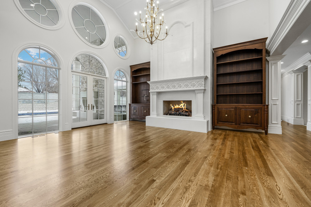 This is an example of an expansive open plan games room in Salt Lake City with white walls, medium hardwood flooring, a standard fireplace, a stone fireplace surround, a built-in media unit, brown floors, a vaulted ceiling and panelled walls.