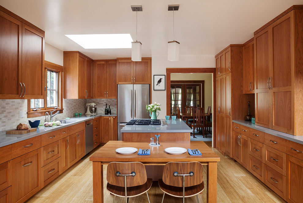 Photo of an arts and crafts u-shaped eat-in kitchen in San Francisco with shaker cabinets, medium wood cabinets, grey splashback, stainless steel appliances, light hardwood floors, with island and beige floor.