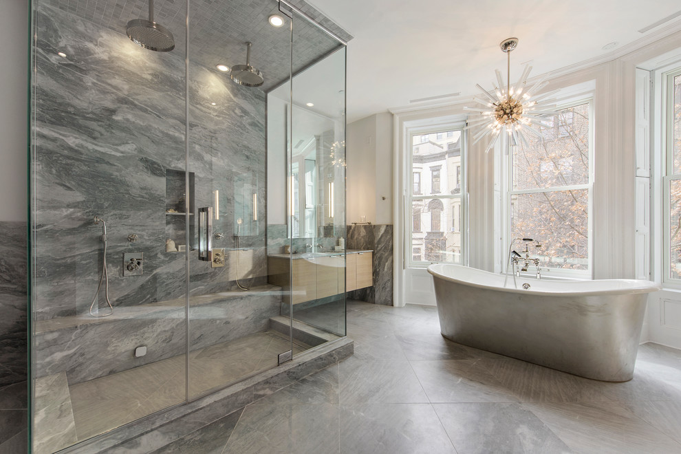 Contemporary master bathroom in New York with flat-panel cabinets, light wood cabinets, a freestanding tub, a double shower, gray tile, marble, grey floor and a hinged shower door.